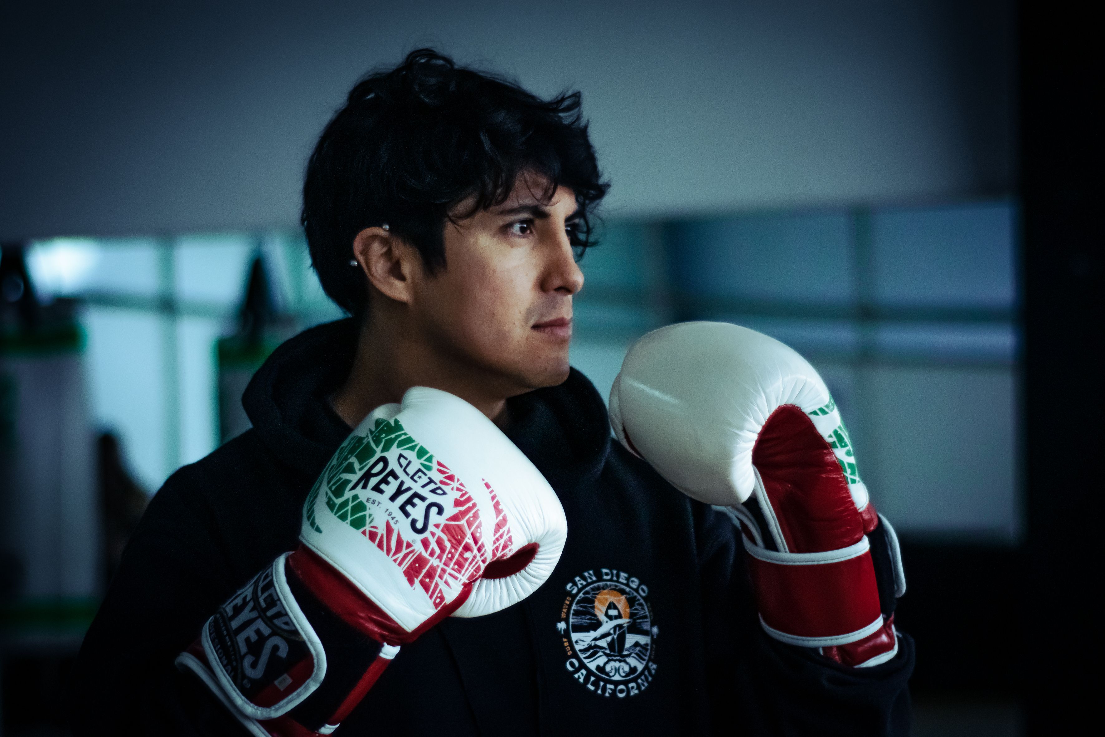 A focused young adult boxer in a gym wearing colorful boxing gloves, ready to train.