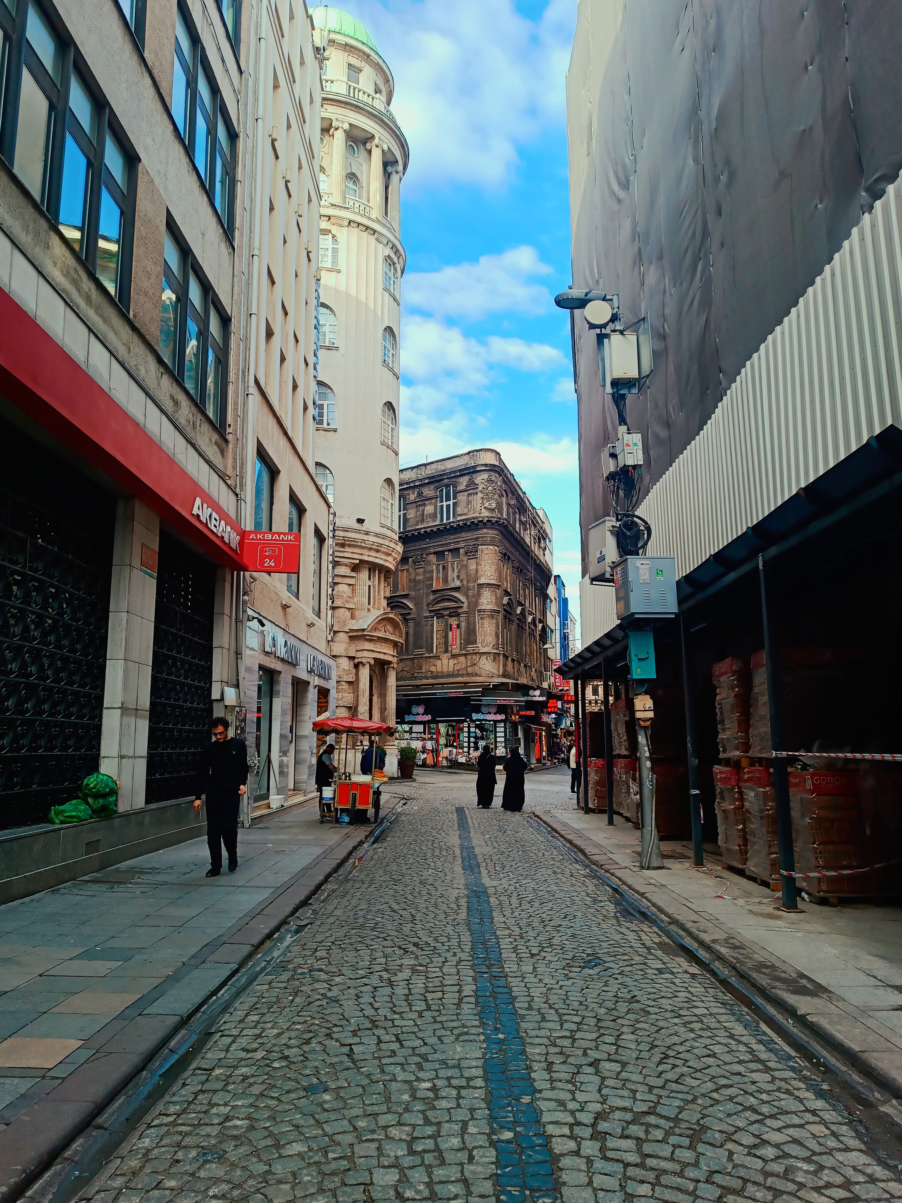 Cobblestone street flanked by historic and modern buildings under a blue sky.