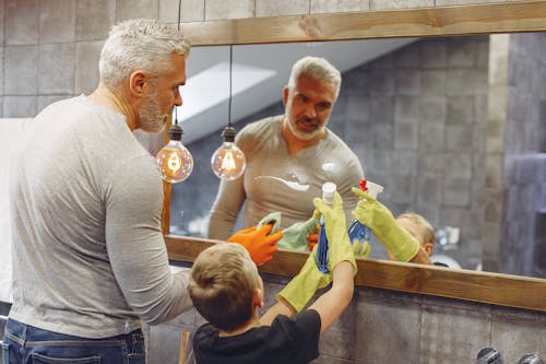 Free Back view of small kid helping grey haired father with beard cleaning in bathroom Stock Photo