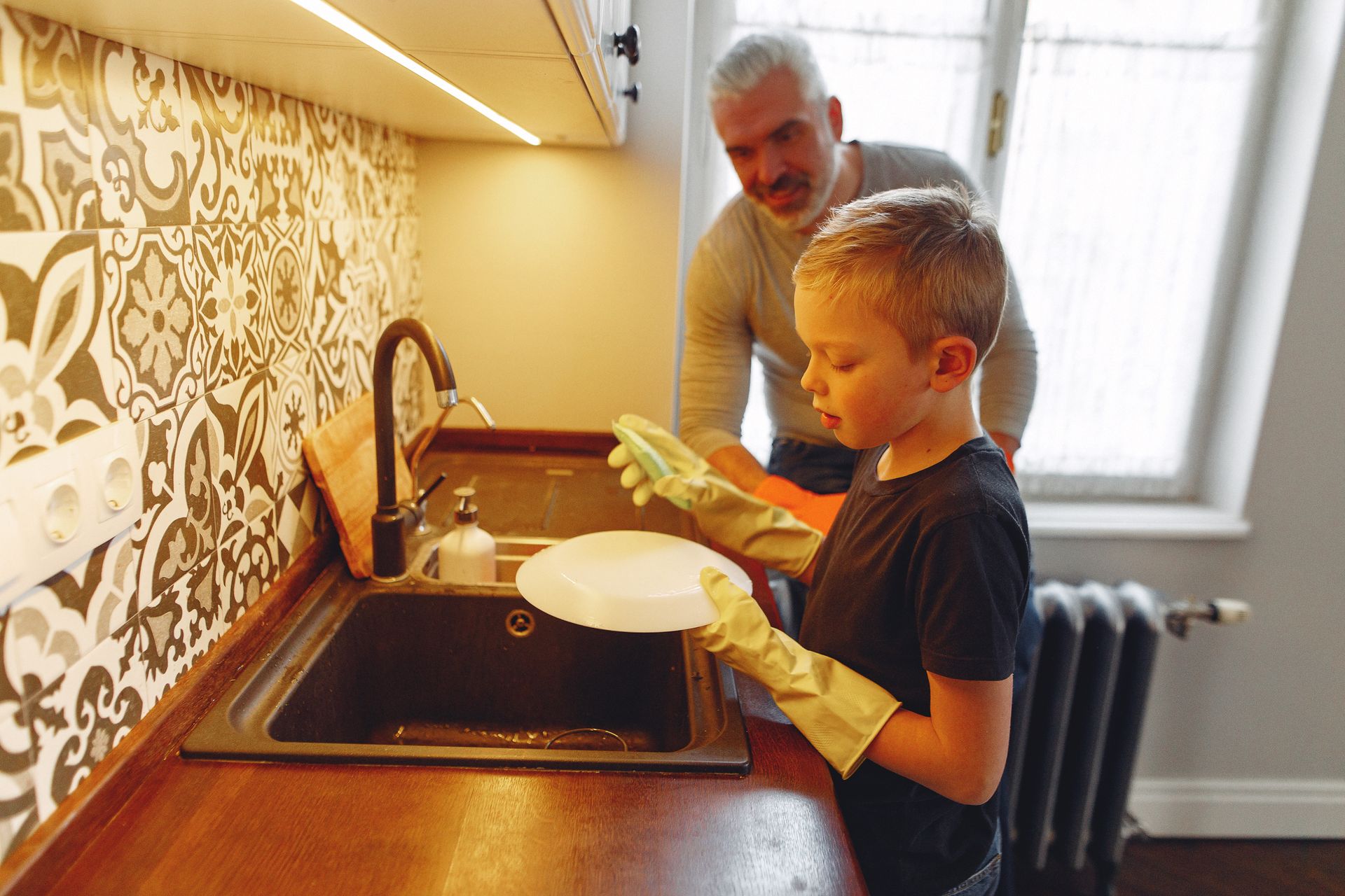 Father and son bonding while washing dishes together in a cozy kitchen setting.