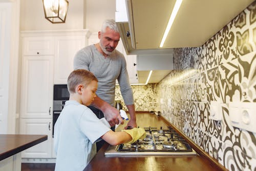 Father with son cleaning stove at kitchen