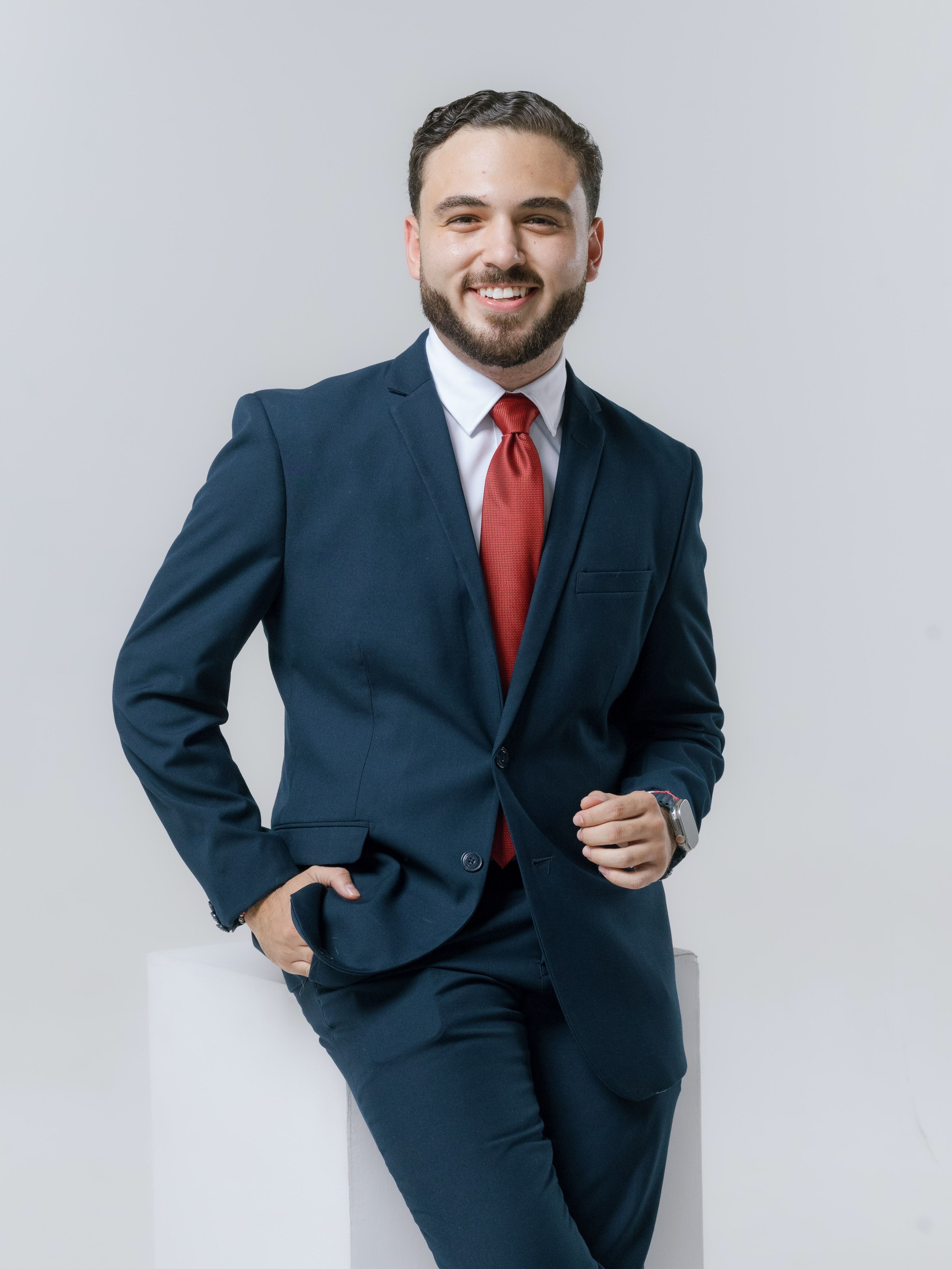 Confident young man in a blue suit with a red tie, smiling.