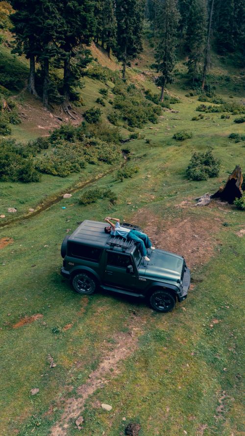 Free Person relaxing on a jeep amidst the scenic Kashmir wilderness. Stock Photo
