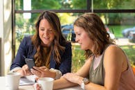 两位女士在舒适的咖啡馆里边看手机边讨论商业想法