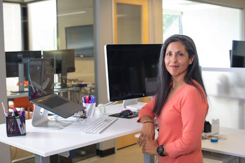 A Woman Wearing a Pink Top Leaning on a Desk