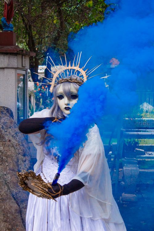 Free A captivating image of a figure in elaborate costume releasing blue smoke, set in a vibrant outdoor environment. Stock Photo