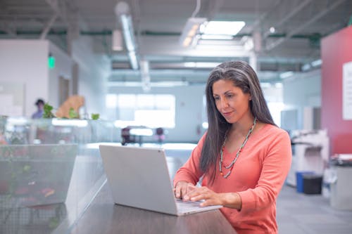 使用macbook Pro的橙色長袖襯衫的女人