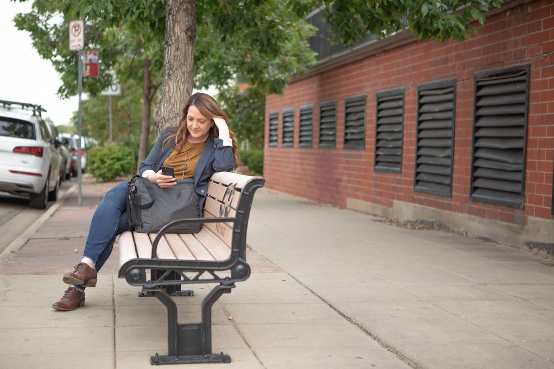 A Woman Browsing Her Smartphone while Sitting on a Bench