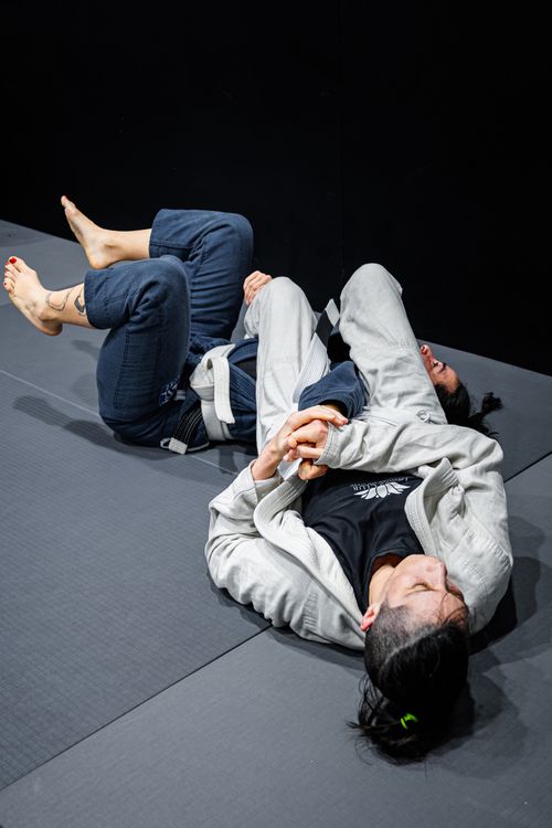 Free Two women engaged in a Brazilian Jiu-Jitsu sparring session on mats indoors. Stock Photo