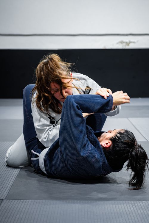 Free Women practicing Brazilian jiu-jitsu grappling on a mat indoors. Intense focus and technique in action. Stock Photo