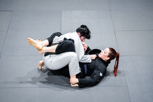 Free Dynamic grappling between two women practicing Brazilian Jiu-Jitsu on a mat. Stock Photo