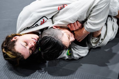 Free Women practicing Brazilian Jiu-Jitsu on a gym mat, showcasing intense combat sports action. Stock Photo