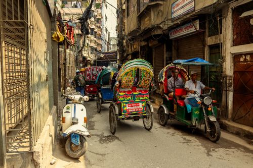 Free Colorful rickshaws and a scooter navigate a bustling alley in Dhaka, Bangladesh. Stock Photo