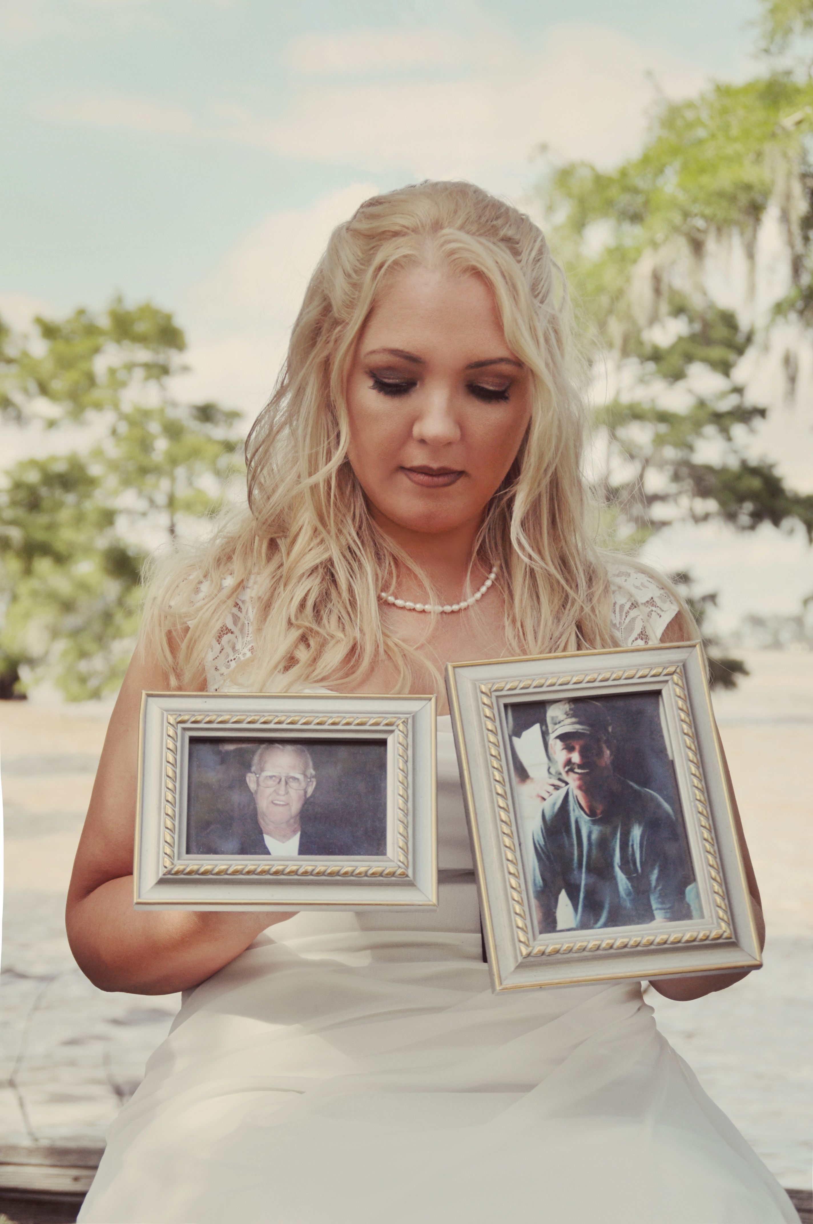 Bride holding framed photos, honoring departed loved ones during her outdoor wedding in Louisiana.