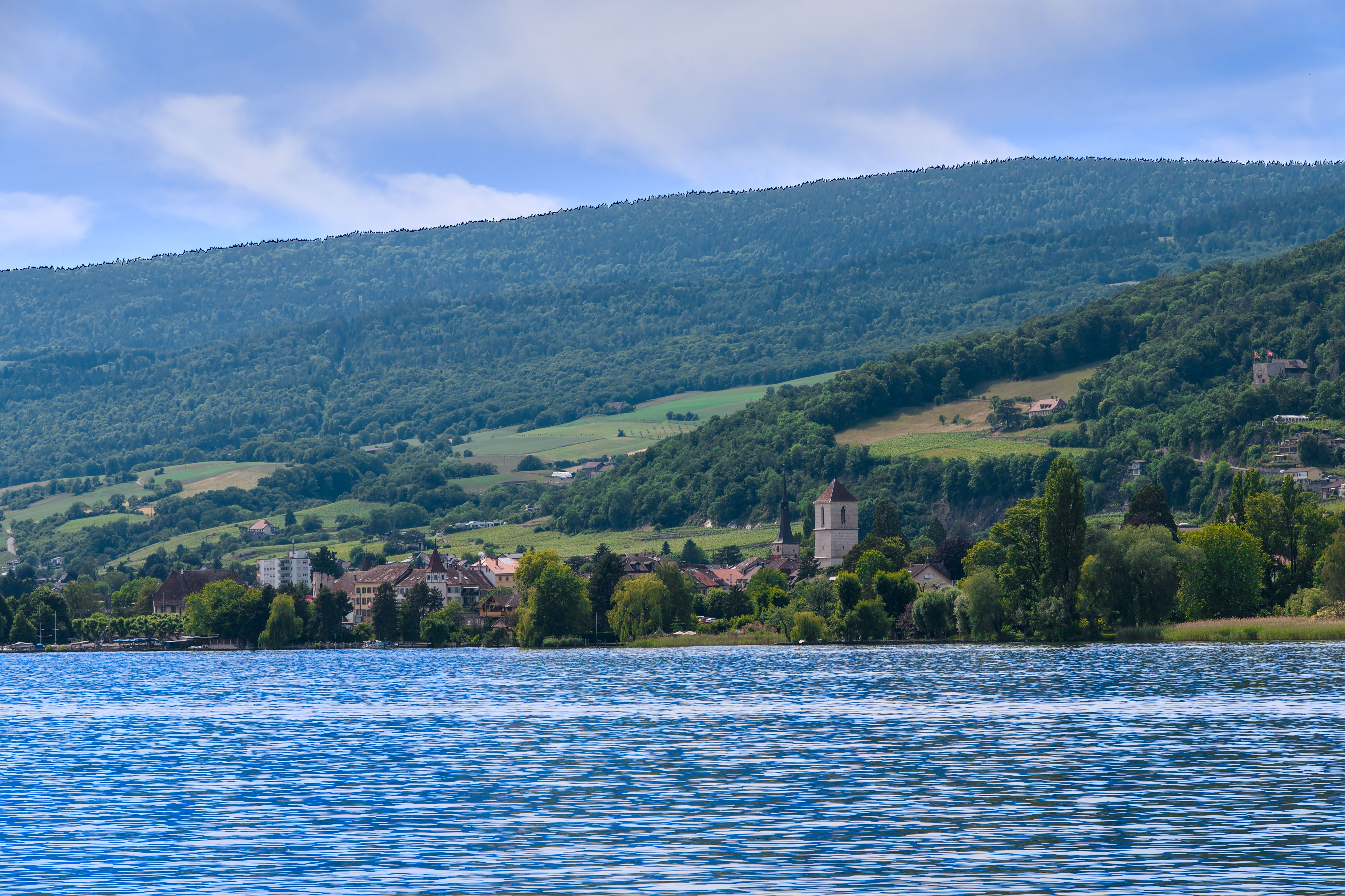 Idyllic Swiss village with church by Lake Neuchâtel under lush green hills.