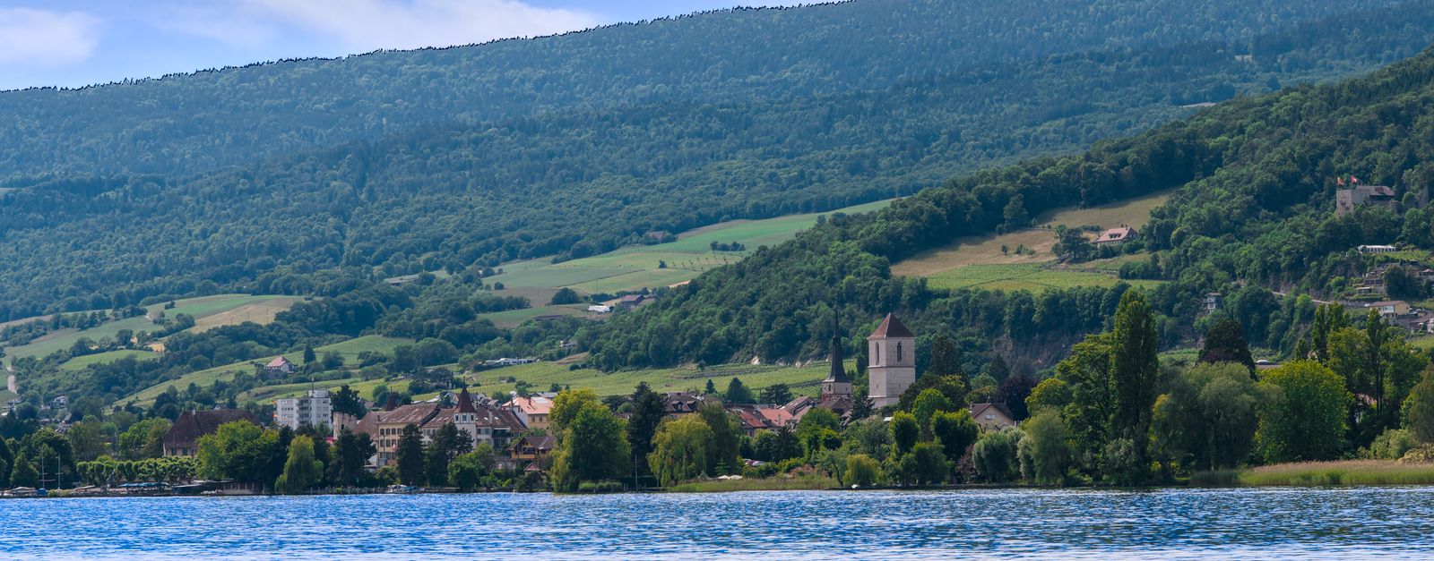 Idyllic Swiss village with church by Lake Neuchâtel under lush green hills.