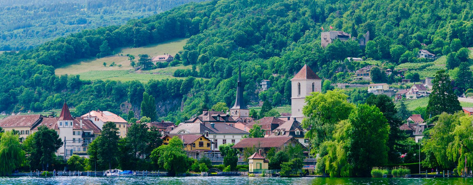 Scenic view of a village by Lake Biel in Swiss countryside, surrounded by lush hills.