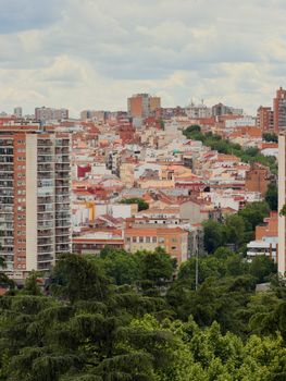 A vibrant cityscape view of Madrid showcasing residential buildings and lush greenery under a cloudy sky.