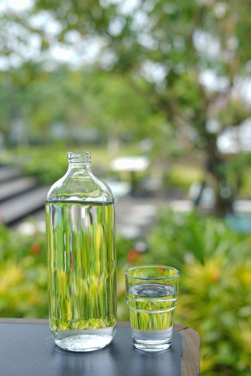 Free Clear glass and bottle of water sitting on a table in a vibrant outdoor setting. Stock Photo