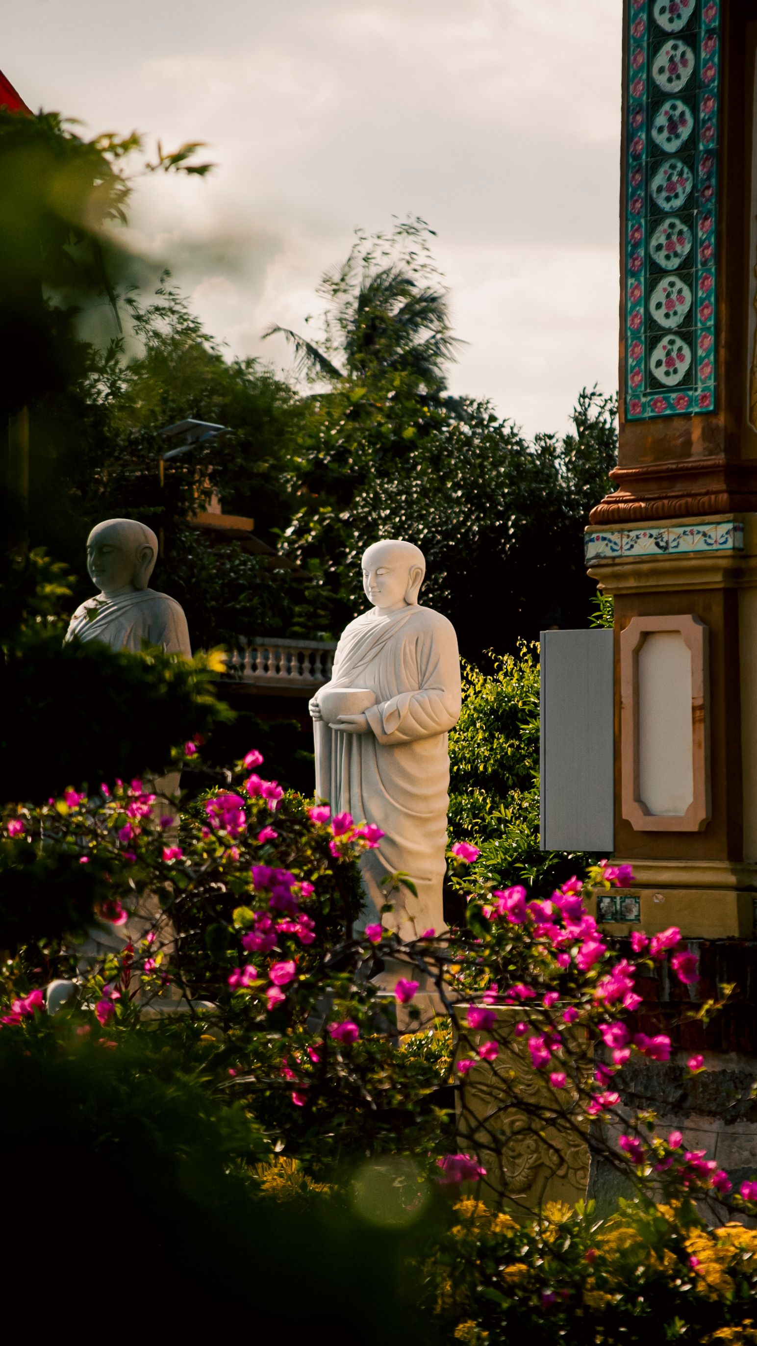 Peaceful Buddhist statues in a vibrant floral garden at sunset in My Phong, Vietnam.