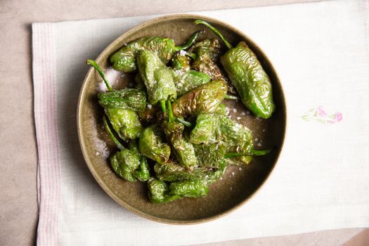 Tasty fried Padron peppers served with salt on a rustic plate.