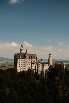 A breathtaking view of the iconic Neuschwanstein Castle surrounded by lush greenery under a clear sky.