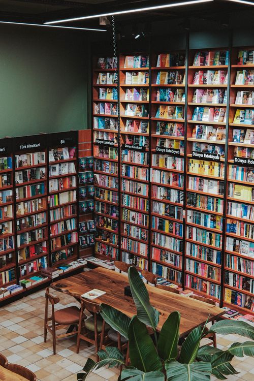 Free A cozy bookstore with tall shelves filled with books and a wooden reading table. Stock Photo