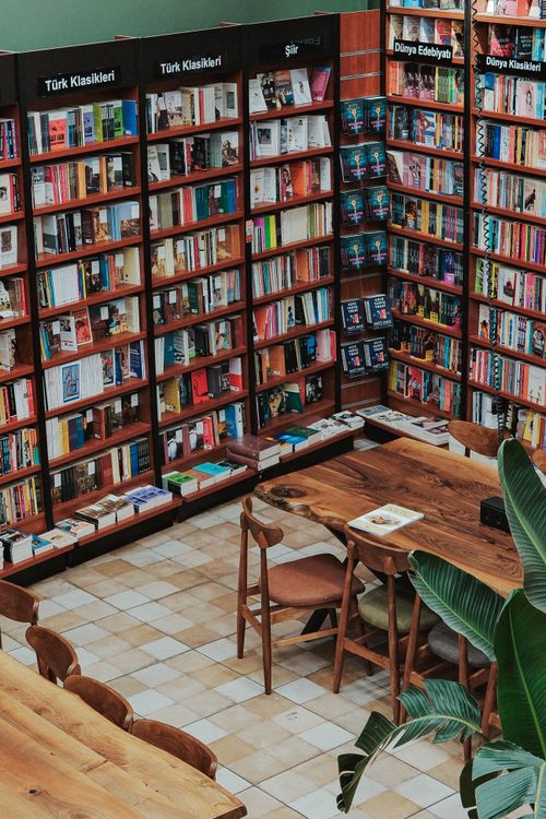 Free Inviting bookstore interior with wooden tables surrounded by shelves of diverse books. Stock Photo