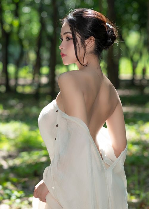 Free A graceful woman in a white dress posing outdoors in a sunlit forest, capturing elegance and natural beauty. Stock Photo