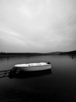 A solitary boat floats on a calm lake under an overcast sky, creating a dramatic and serene scene.