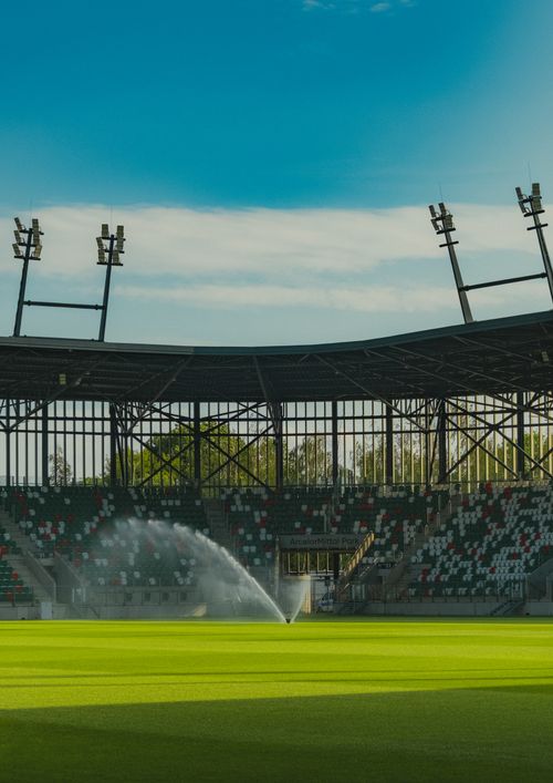 Free Wide view of a modern sports stadium with green field and water sprinklers in Sosnowiec, Poland. Stock Photo