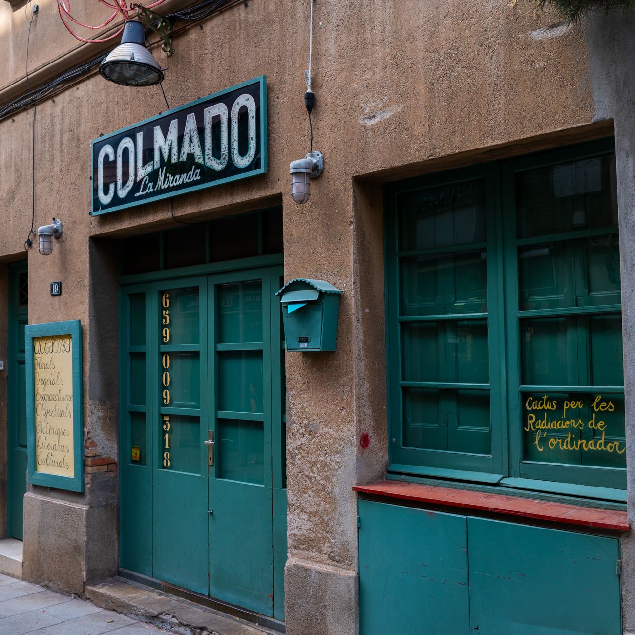Facade of a traditional Spanish colmado with vibrant green doors and signage in an urban street setting.