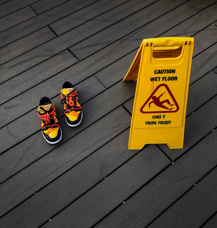 Stylish Sneakers On Wooden Floor Near Caution Board