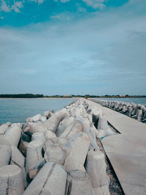 Free Concrete breakwaters line a coastal walkway under a blue sky, creating a serene marine landscape. Stock Photo
