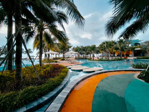 Free A serene tropical resort pool surrounded by palm trees under a clear blue sky. Stock Photo