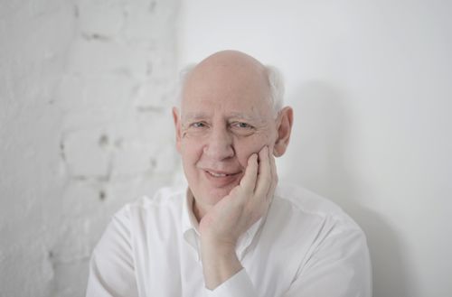 Free A thoughtful elderly man with white hair, resting his face on his hand, dressed in a white shirt. Stock Photo