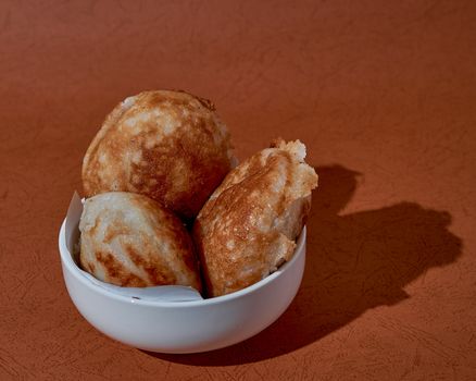 Close-up of appam served in a white bowl on a rustic background, emphasizing texture.
