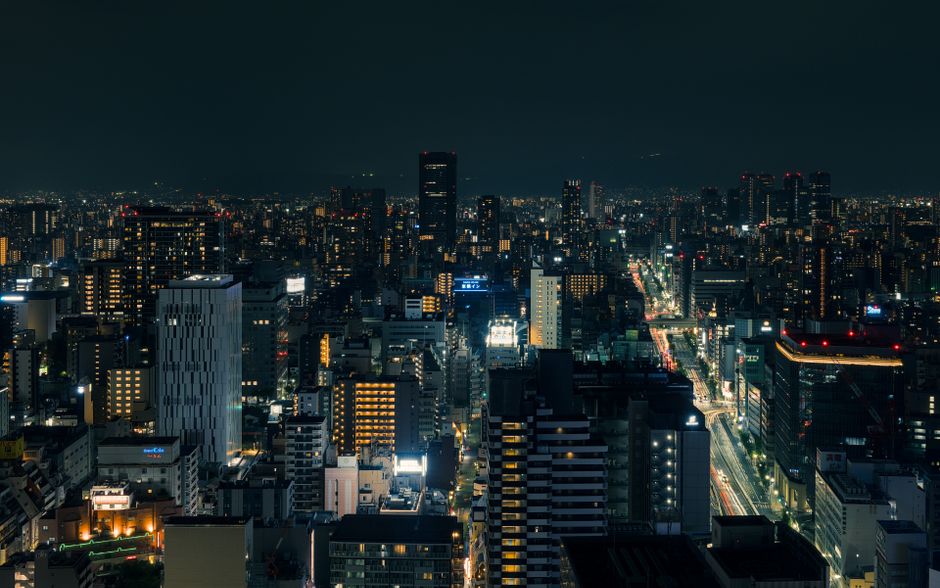 A beautiful nighttime cityscape of Osaka, Japan, with illuminated buildings and streets.
