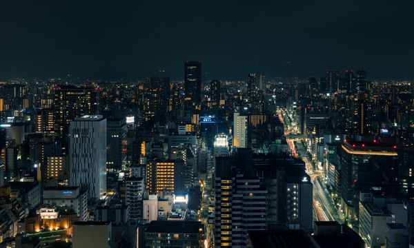 A beautiful nighttime cityscape of Osaka, Japan, with illuminated buildings and streets.