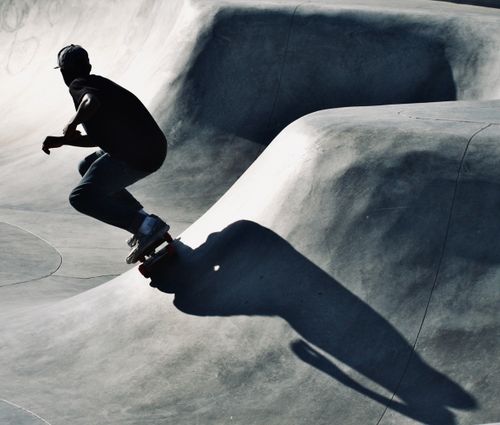 Free Silhouette of a skateboarder in action at a concrete skatepark, casting a dramatic shadow. Stock Photo