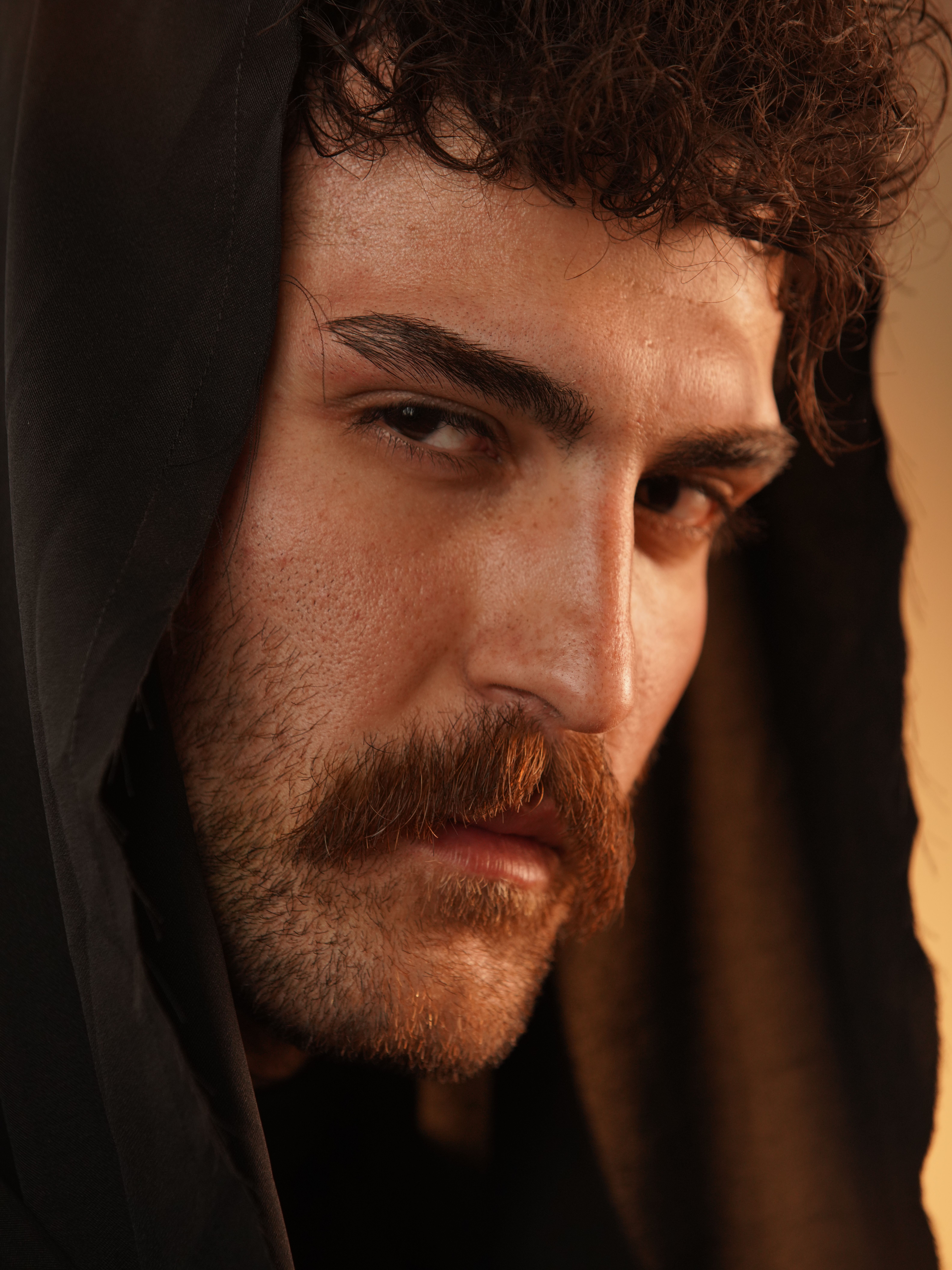 Detailed portrait of a man with a mustache and hooded attire, looking intensely at the camera.