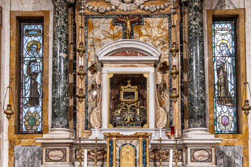 Free Intricate church altar with detailed carvings and illuminated stained glass windows on either side. Stock Photo