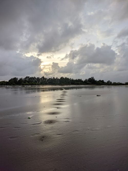 Free Footprints on a tranquil beach at sunrise, featuring reflective wet sand and a dramatic sky. Stock Photo