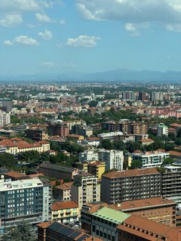 Aerial view of Milan's urban architecture on a bright day with distant mountains.