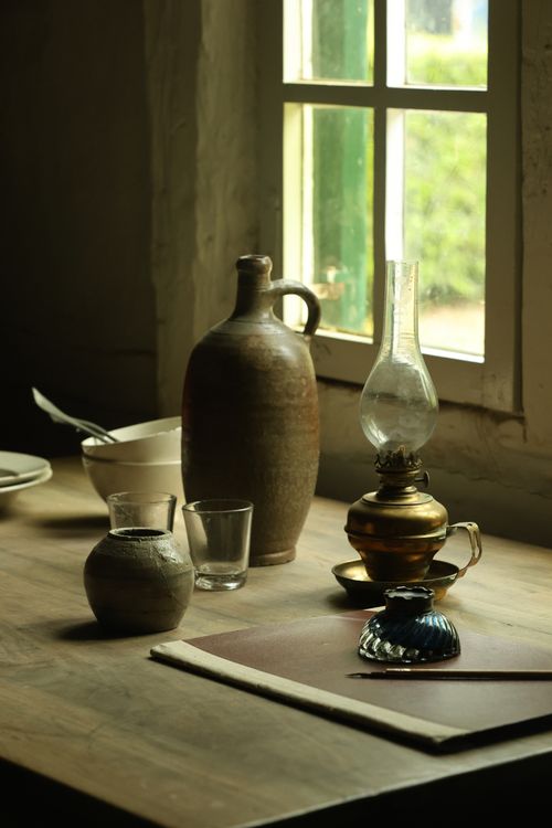 Free A rustic still life showcasing pottery, an oil lamp, and rustic tableware in sunlight. Stock Photo