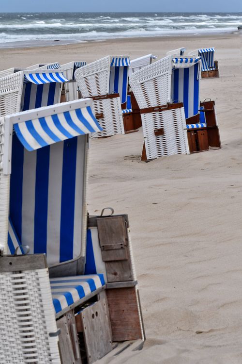 Free Rows of blue and white striped beach chairs on a sandy shore evoke a serene summer day. Stock Photo