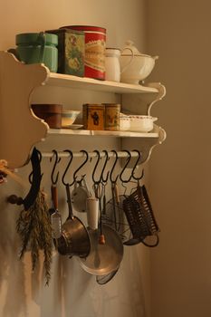 Rustic kitchen shelf with vintage tins and hanging cookware, warm tones.