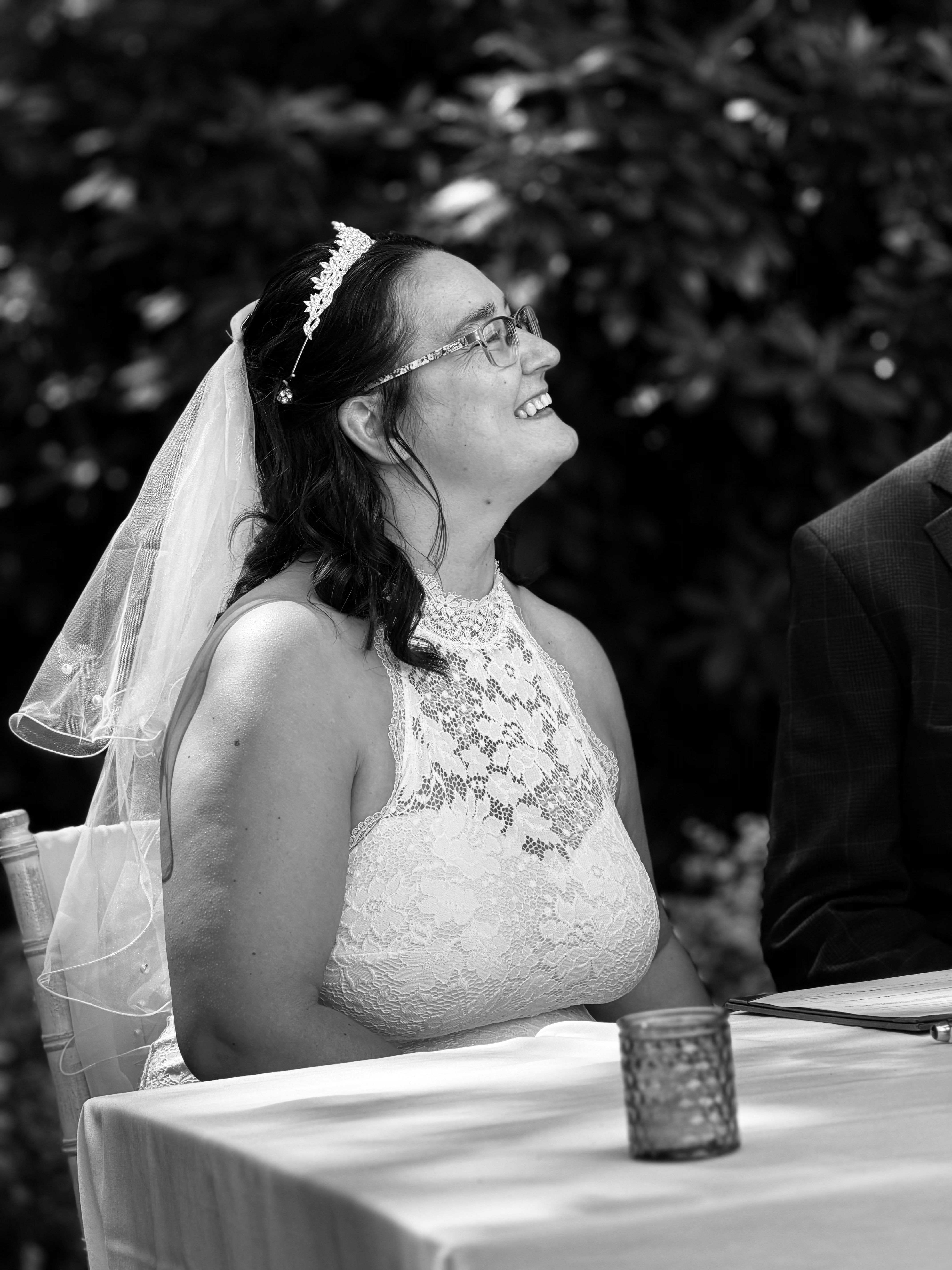 Black and white photo of a smiling bride in a lace dress and veil during a summer wedding.