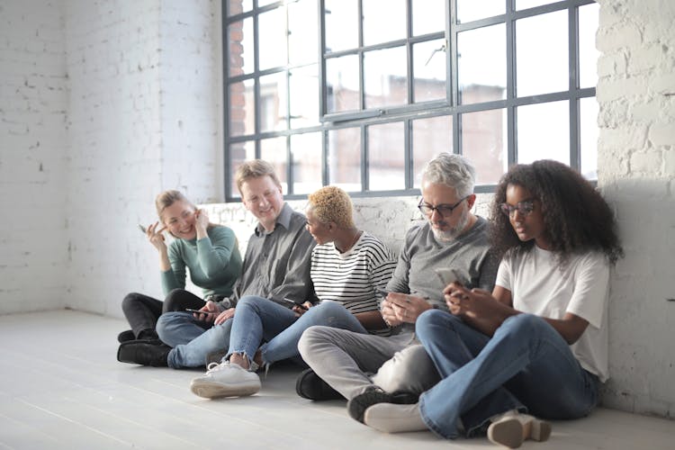 Happy Multiracial Colleagues Sitting On Social Media Using Smartphones