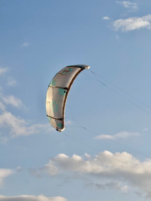 Free A kite surfing parachute gracefully floating against a bright blue sky with scattered clouds. Stock Photo